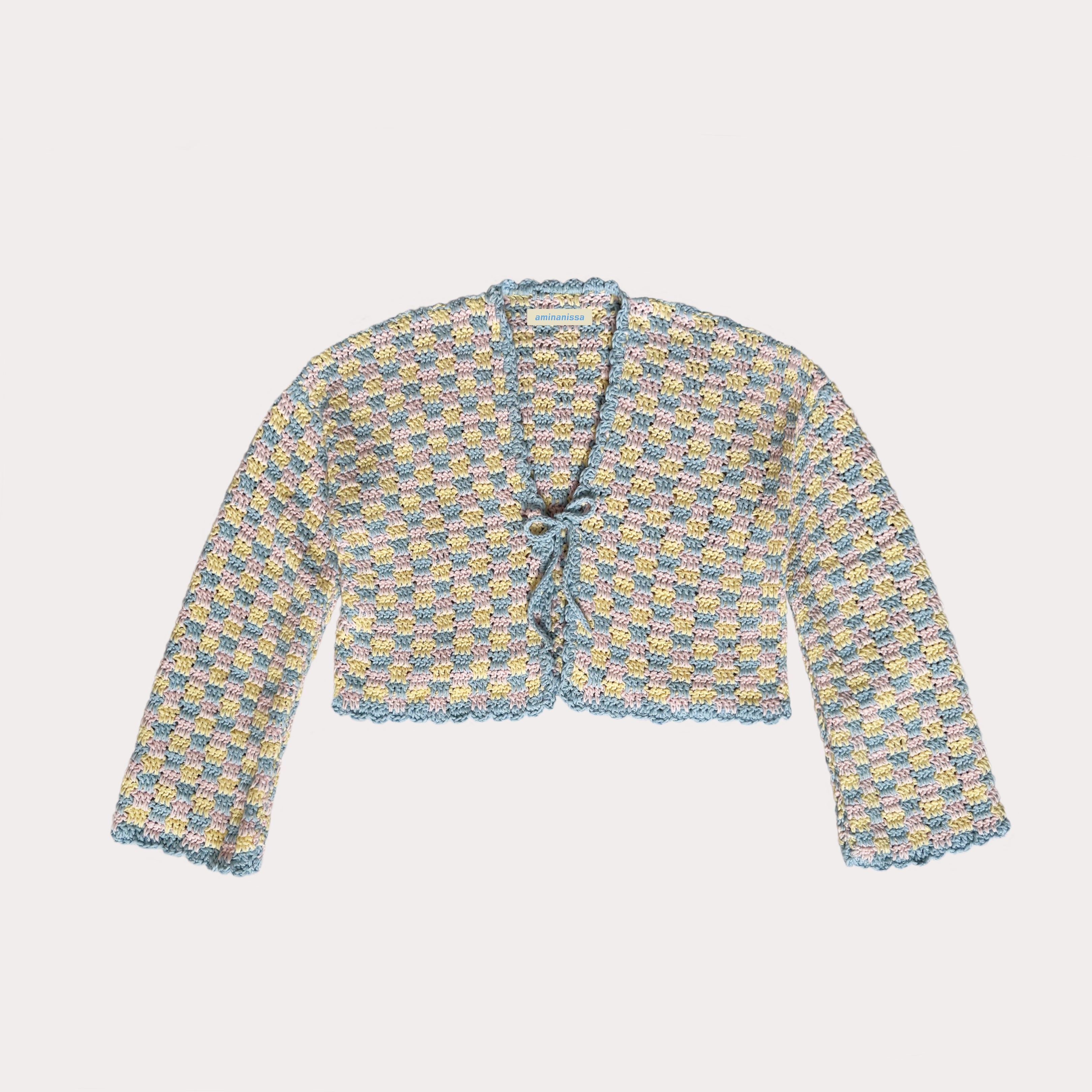 Handgehäkelter, kurz geschnittener Cardigan von aminanissa in Pastellfarben. Die Strickjacke zeigt ein kleinteiliges Karomuster in Hellblau, Gelb und Rosa. Vorne ist sie mit einer schmalen Häkelschleife zum Binden versehen. Das Bild zeigt das Produkt flachliegend auf weißem Hintergrund mit sichtbarem Markenlabel im Nacken.